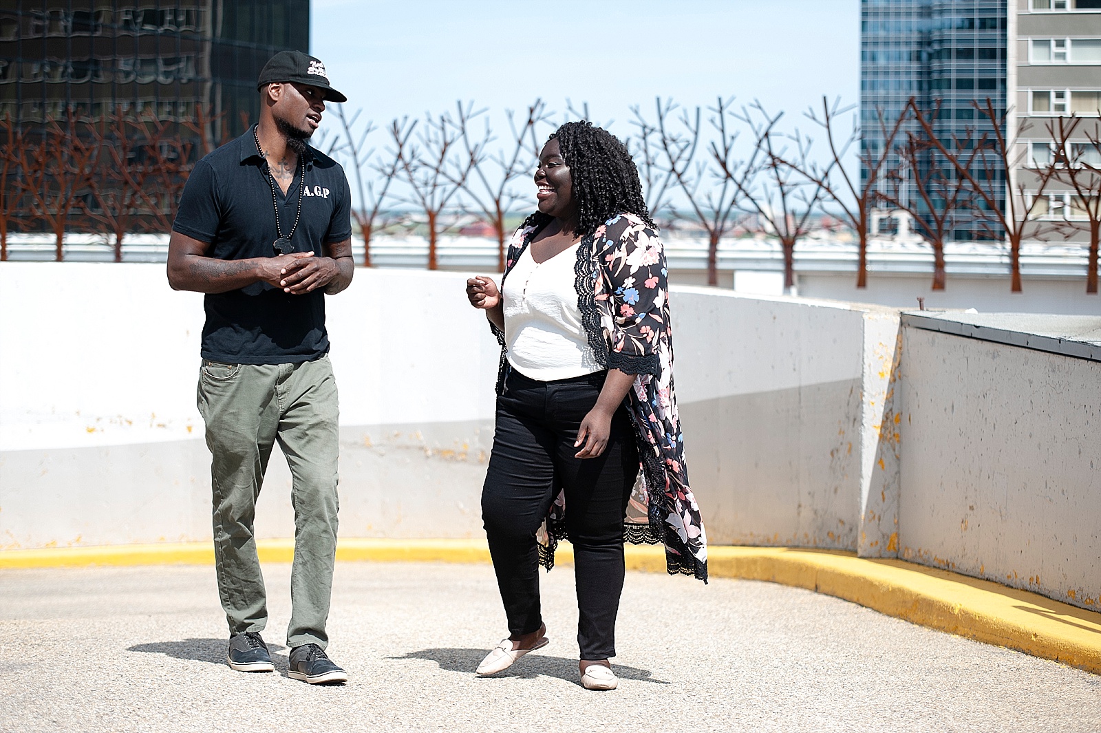 Black woman and Black man laugh as they walk and talk in a downtown Edmonton parkade.